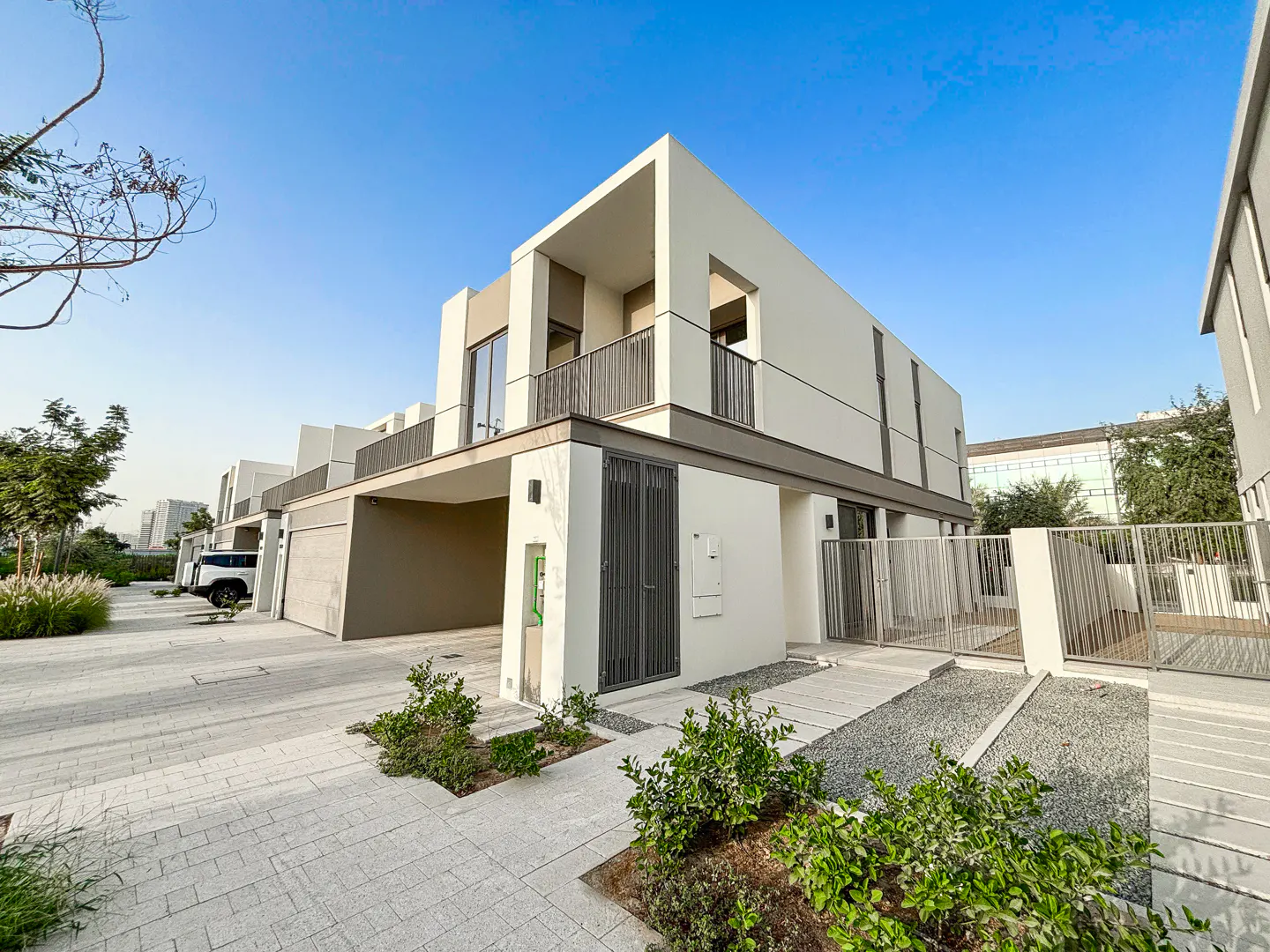 Modern two-story white house with gray trim, balcony, and gated front yard under a clear blue sky.