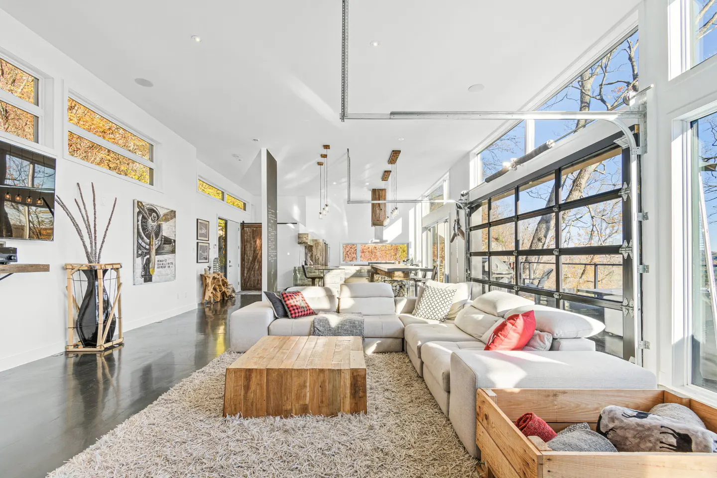 Bright, modern living room with a large sectional sofa, wooden coffee table, and a glass garage door leading to the outside.