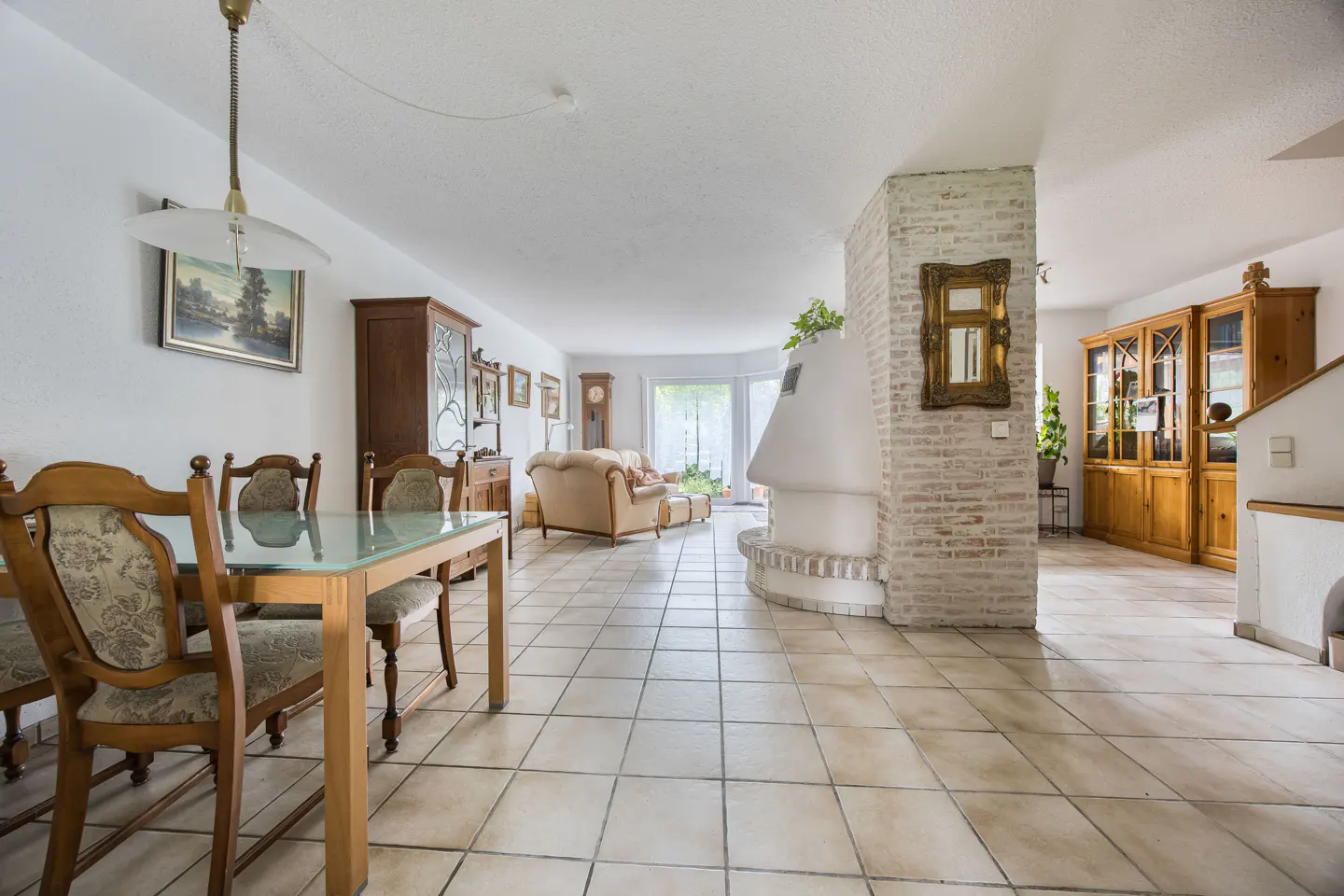 Open-plan living area with tile floors, a glass dining table, a white fireplace, and a beige sofa in the background.