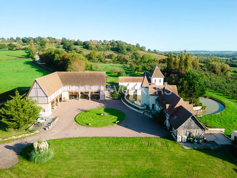 Aerial view of a large, luxurious country estate with a barn, pond, and green lawns under a clear blue sky.