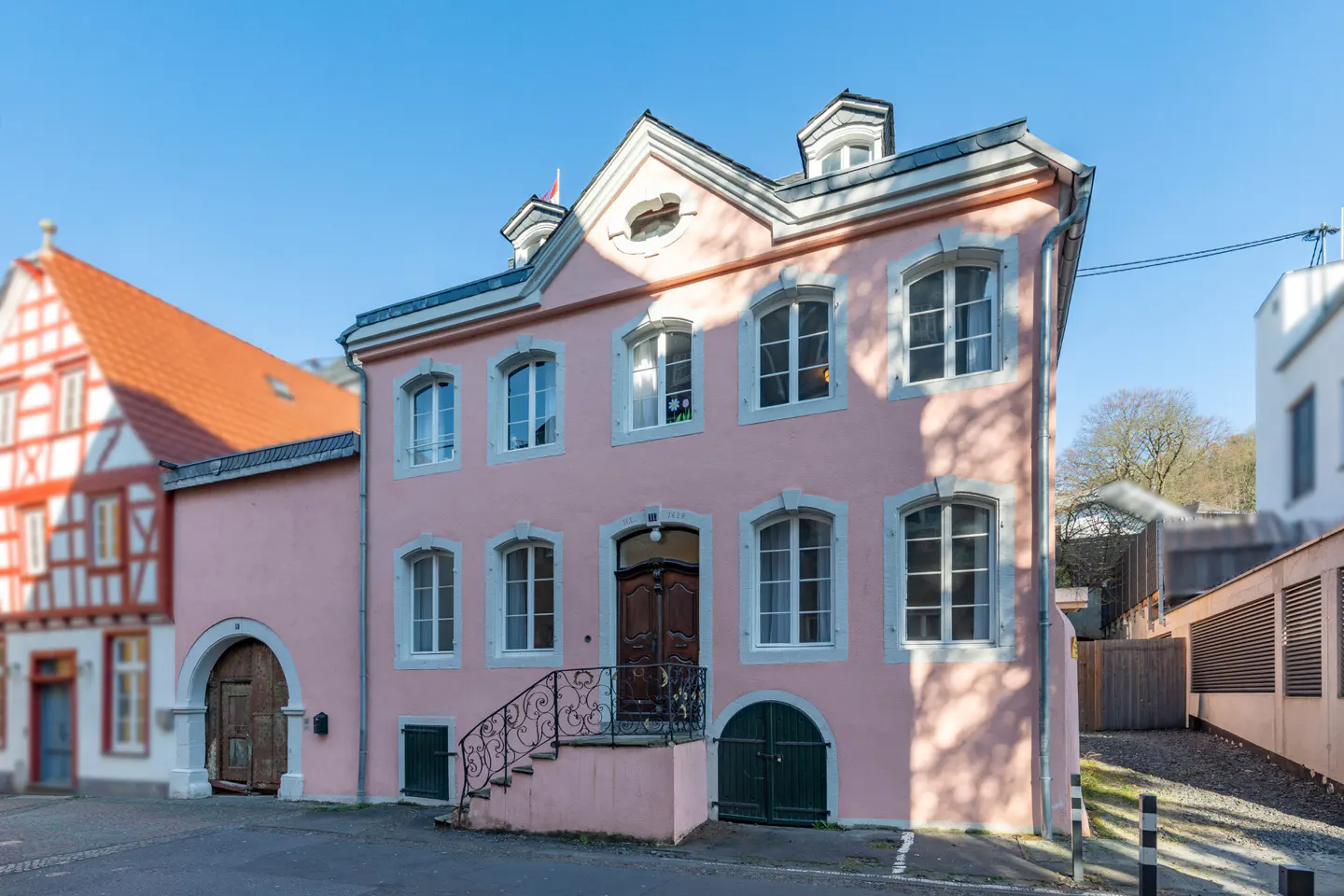 Two-story pink building with white trim and a dark wood door. Stairs with black railings lead to the entrance. Windows are white framed.