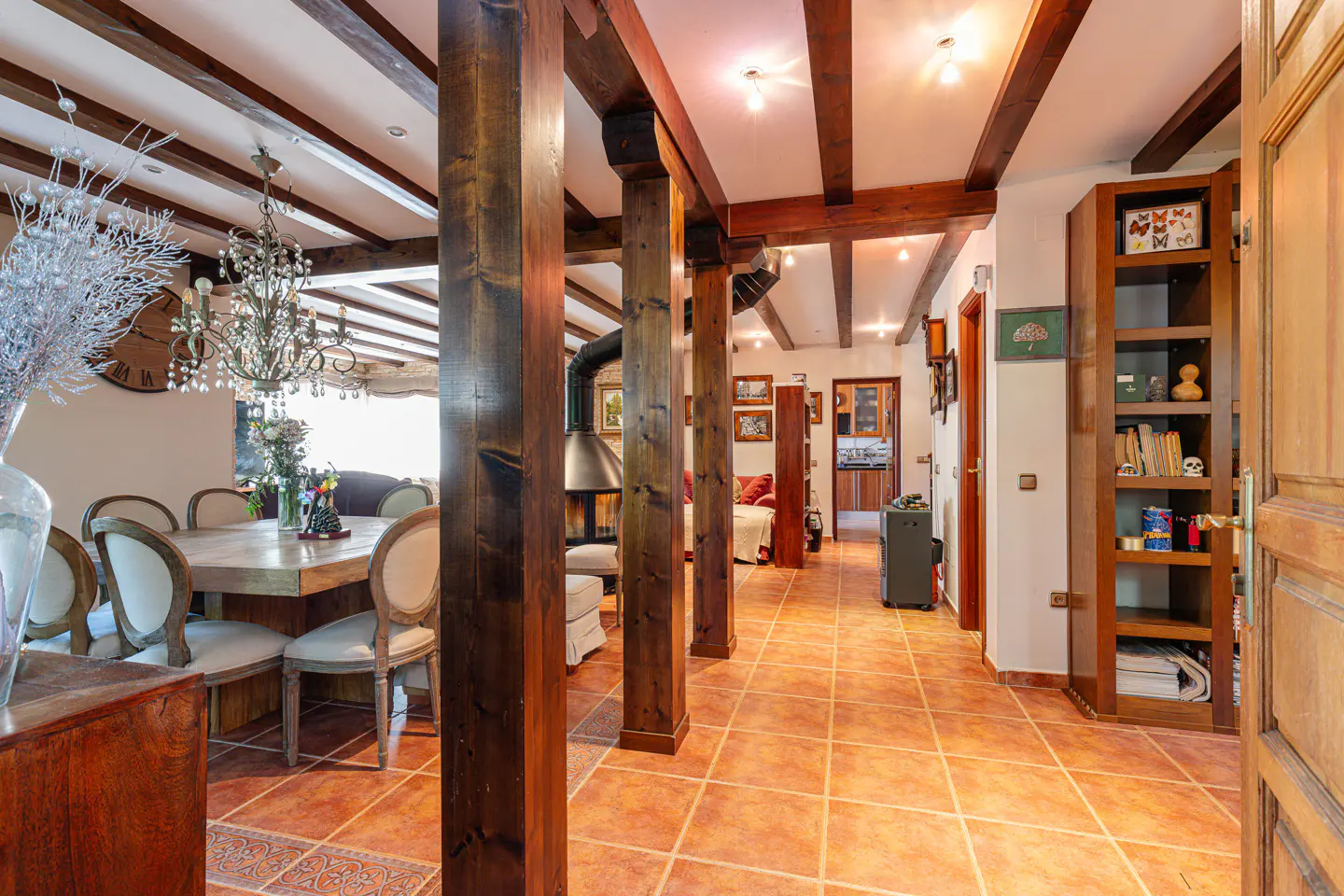 Interior view of a home with exposed wood beams, columns, and terracotta tile flooring. A dining area and living space are visible.