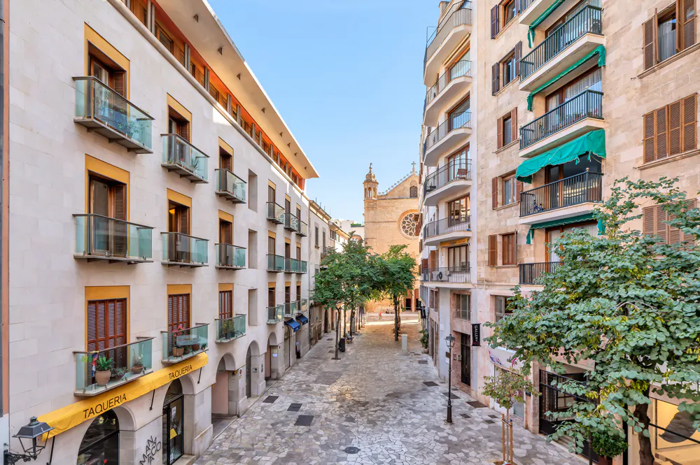 A narrow, stone-paved street in a European city lined with multi-story apartment buildings and a distant stone church.