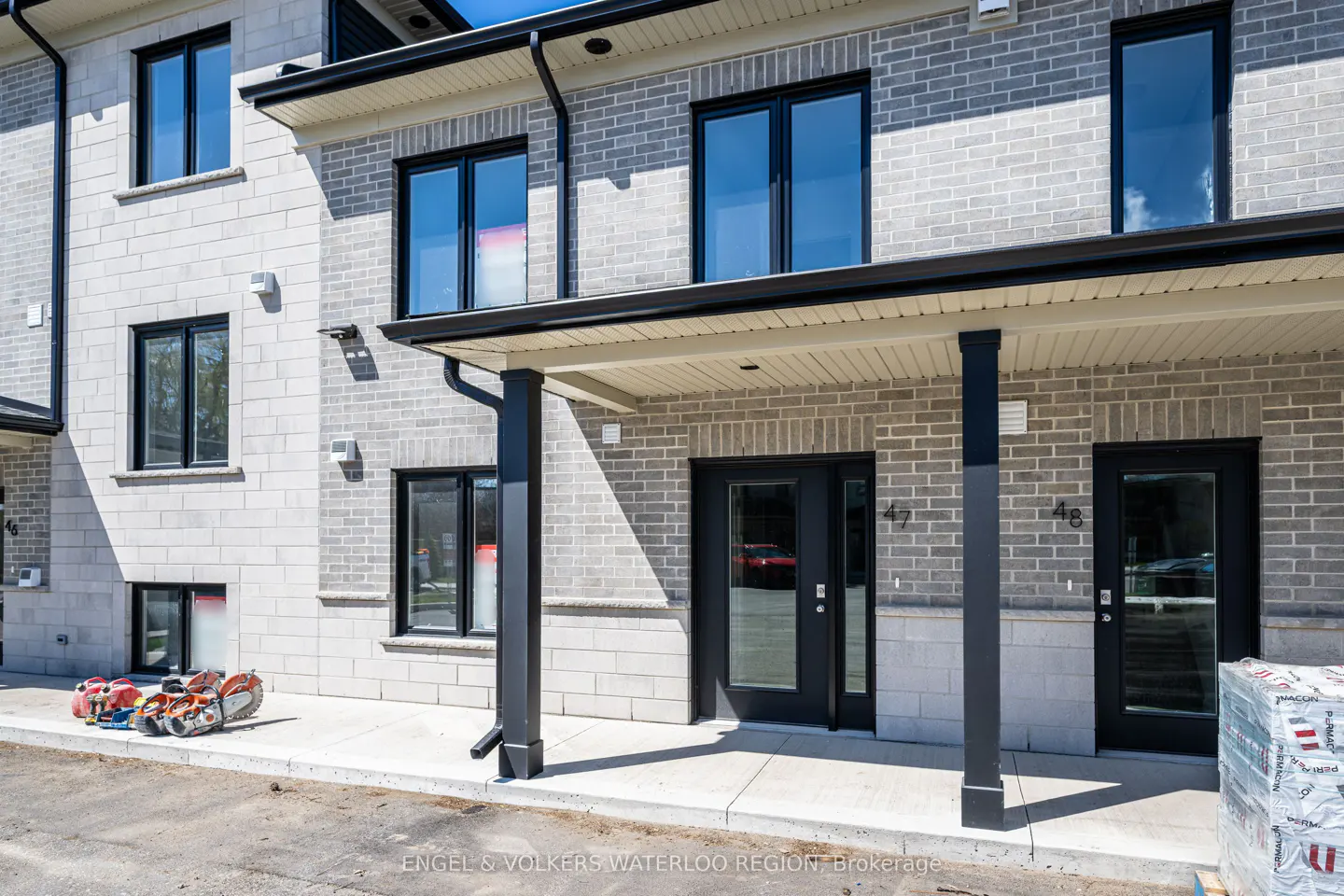 Exterior view of a light gray brick townhouse with black framed windows and doors, numbered 47 and 48. Construction equipment is visible on the ground.