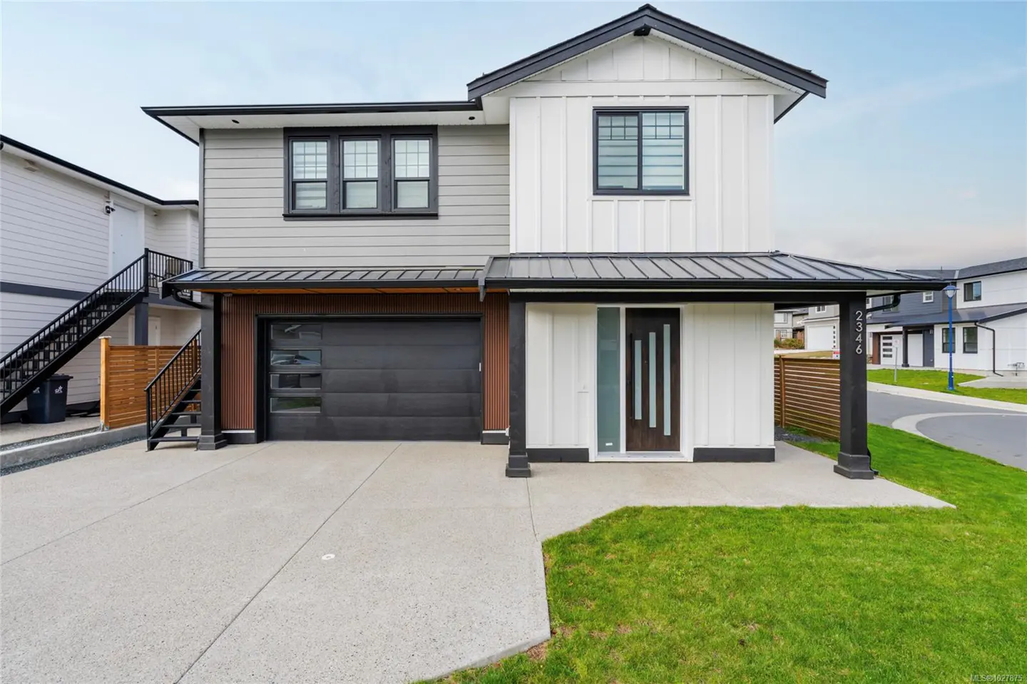 Two-story house with gray and white siding, black trim, a black garage door, and a concrete driveway.