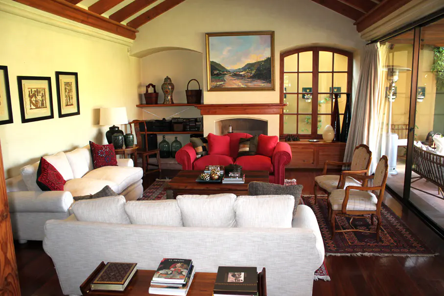 A living room with white sofas, a red loveseat, a fireplace, and a landscape painting above the mantel.