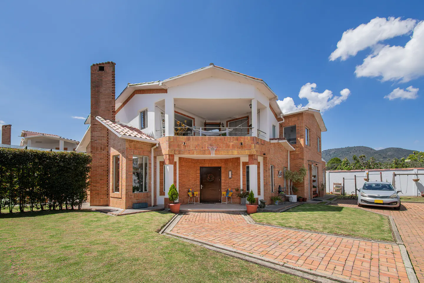 Two-story brick house with white trim, a balcony, and a brick walkway leading to the front door. A car is parked in the driveway.