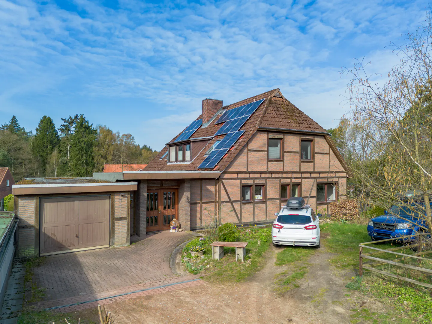 Two-story brick house with solar panels on the roof, a garage, and two cars parked in the yard.