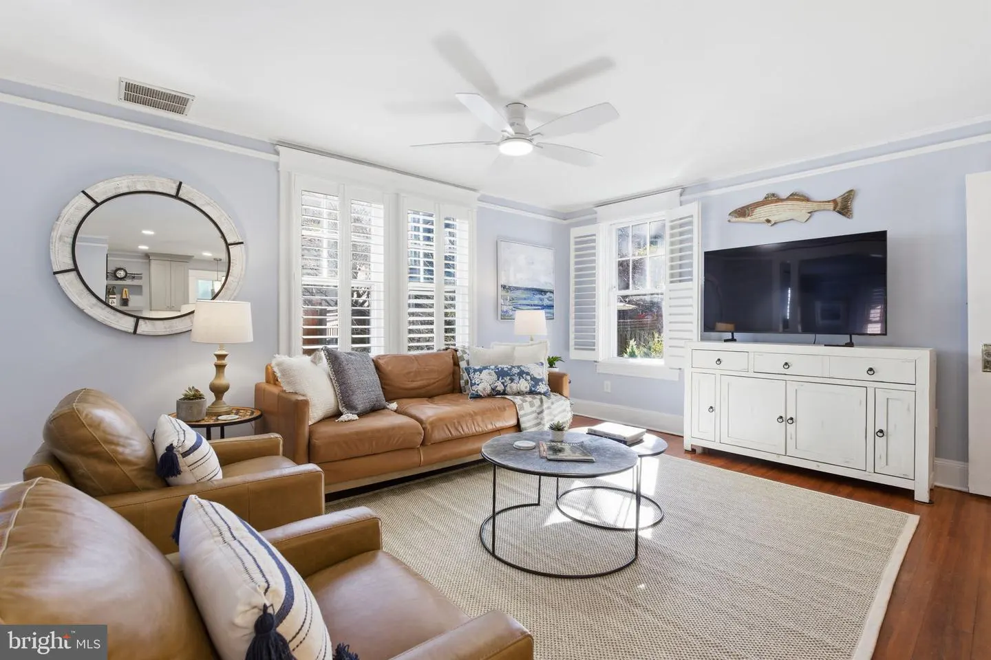 Living room with brown leather sofa and chairs, round coffee tables, and a white media console with a large TV.