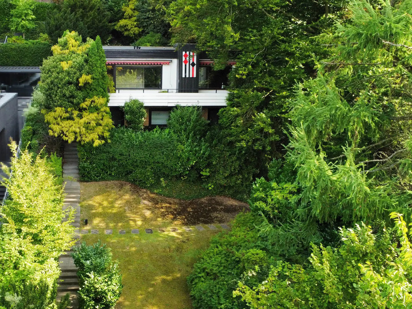 Two-story house with white and black exterior, surrounded by lush green trees and a lawn. A stone path leads to the house.