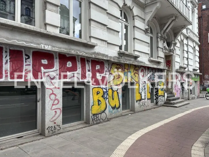 Exterior of a white stone building with large windows, featuring extensive red and yellow graffiti on the ground floor.