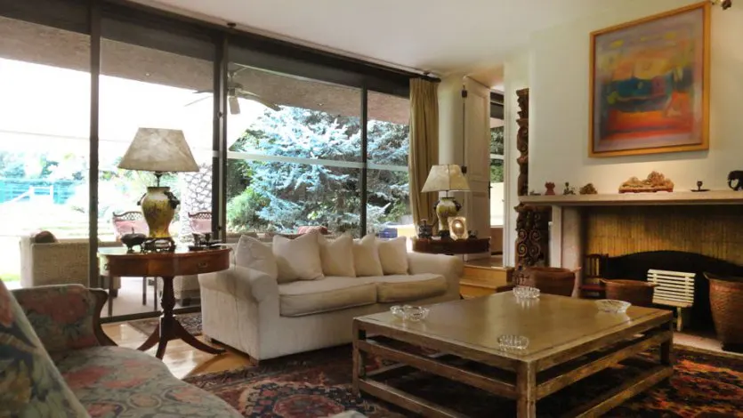 Living room with a white sofa, wooden coffee table, fireplace, and large windows overlooking a garden.