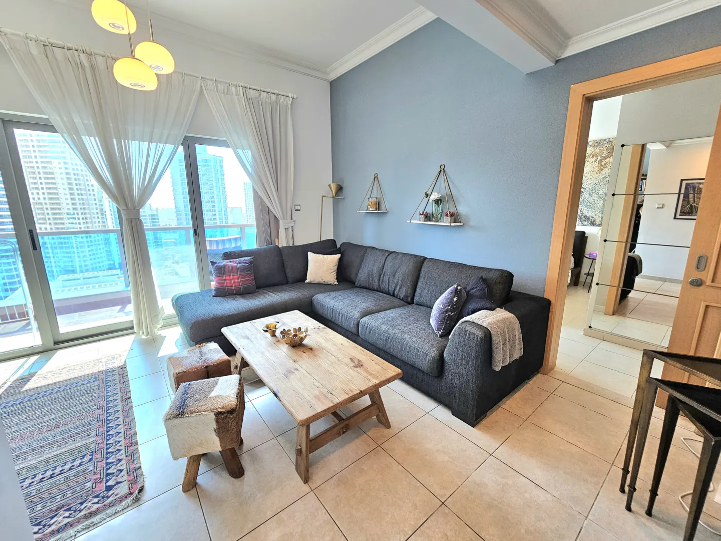 Living room with a gray sectional sofa, rustic wood coffee table, and city view through sheer curtains.