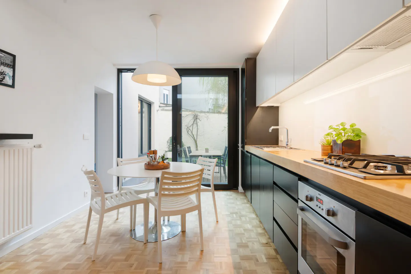 Bright kitchen with white walls, parquet floor, and black cabinets. A round table with white chairs sits near a glass door to a patio.