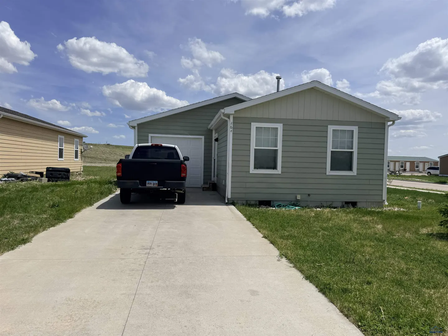 Single-story sage green house with a concrete driveway, attached garage, and a black pickup truck parked in front.