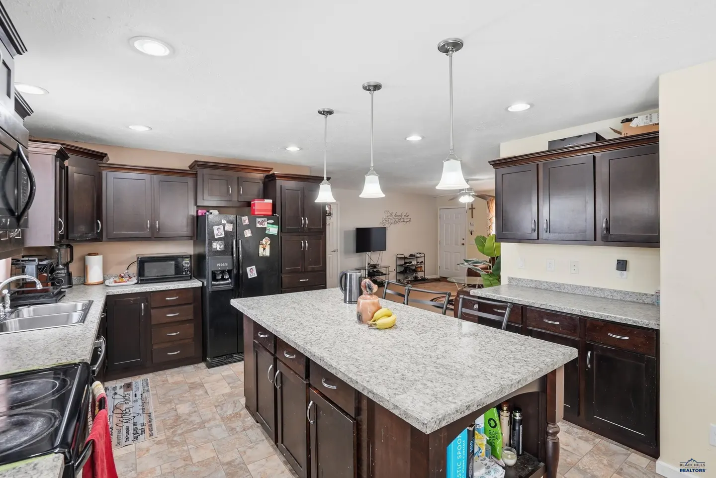 A kitchen with dark wood cabinets, granite countertops, and a central island with pendant lighting.