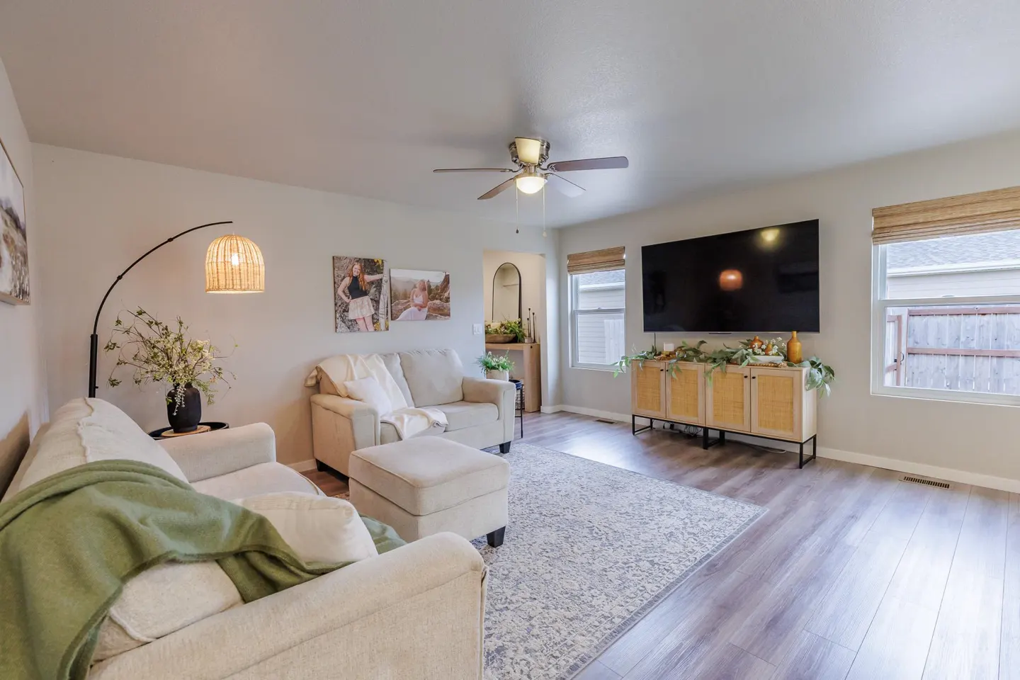 Living room with beige sofas, a patterned rug, and a large TV on a wooden cabinet. A floor lamp and family photos add a personal touch.
