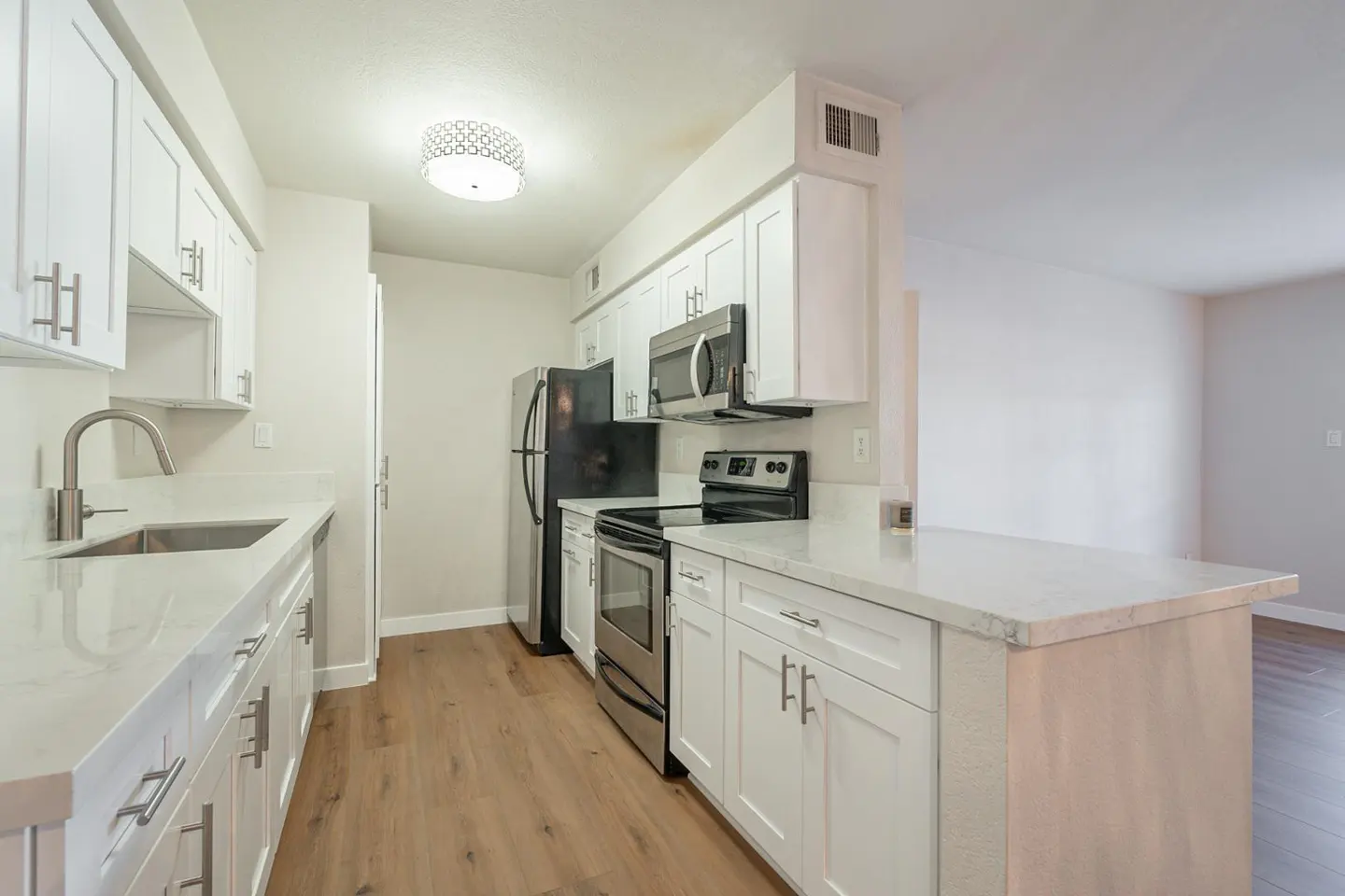 Bright kitchen with white cabinets, stainless steel appliances, and wood-look flooring. A black refrigerator stands near the stove.