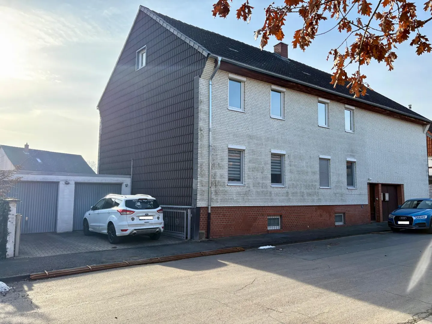 Exterior of a three-story house with a white car parked in front of a garage. A blue car is parked on the street.