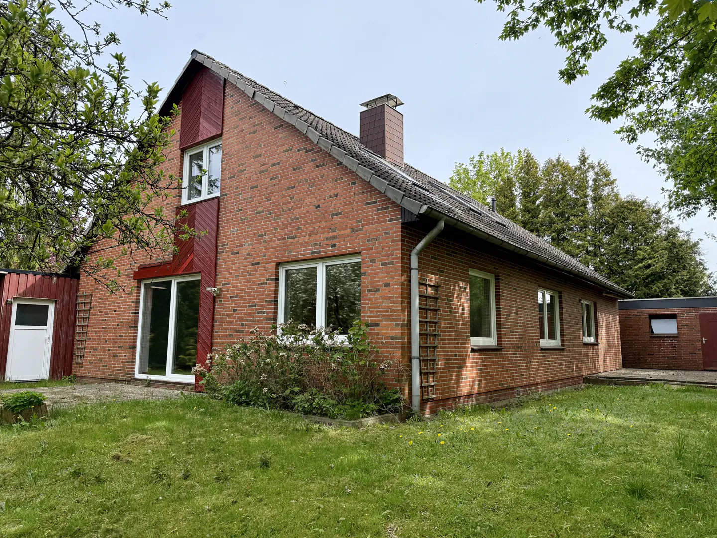 A red brick house with a chimney and a gray roof, surrounded by green grass and trees.