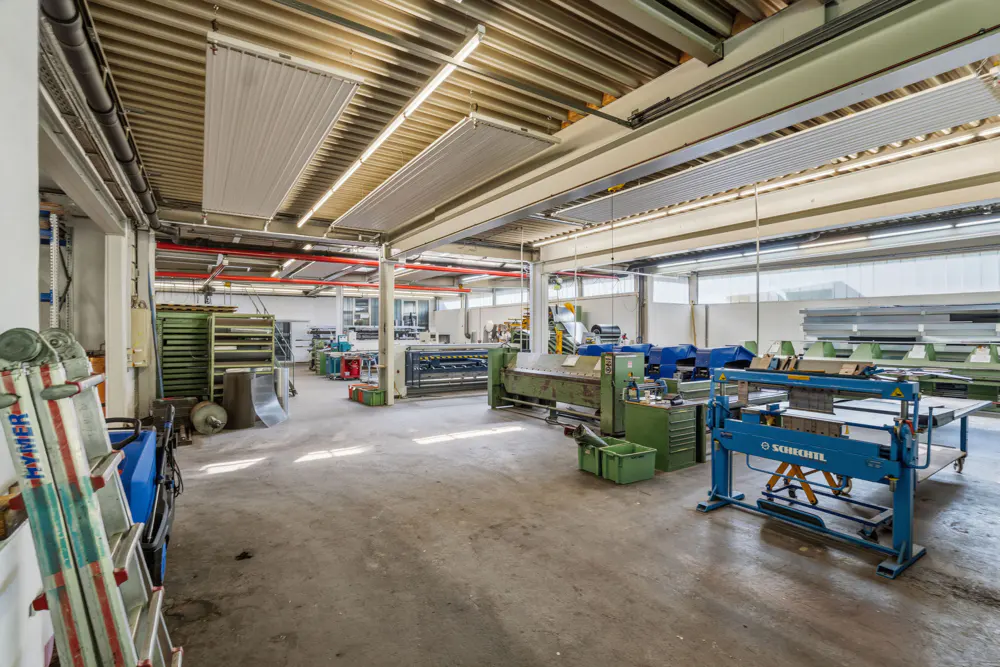Spacious industrial workshop with concrete floors, metal machinery, and high ceilings with exposed beams and lighting.