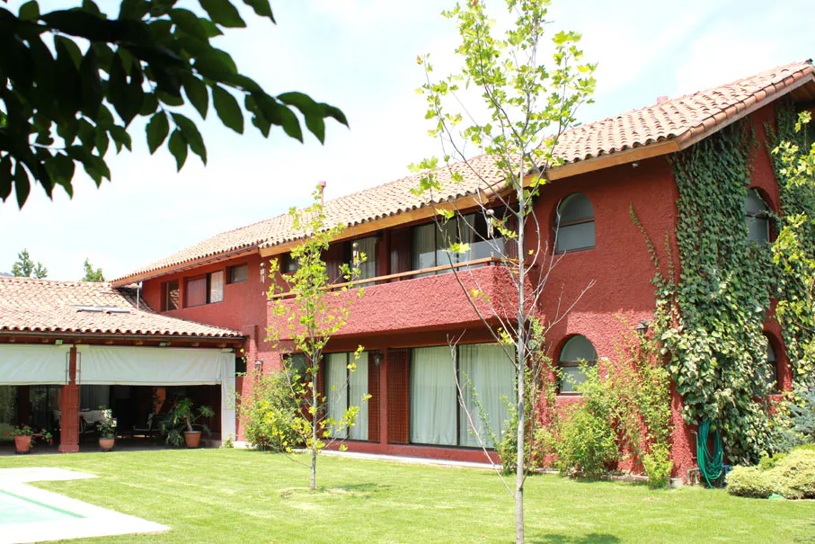 Exterior view of a two-story red house with a terracotta tile roof and green lawn. Vines climb the walls.