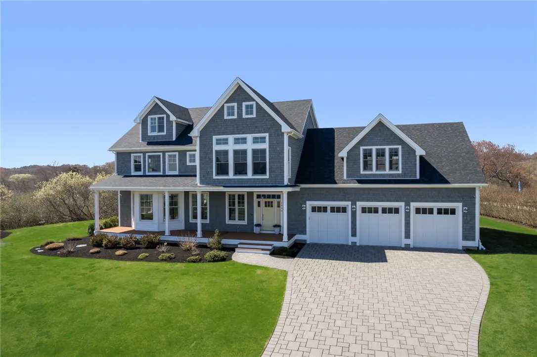 Two-story gray house with white trim, a porch, and a three-car garage on a green lawn.