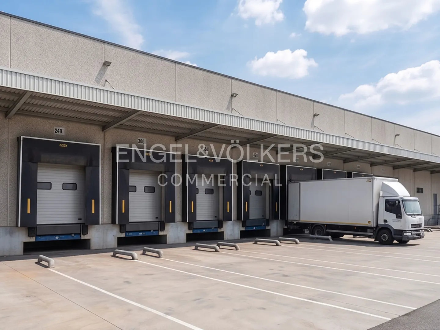 Commercial building with loading docks and a white truck parked outside on a sunny day.