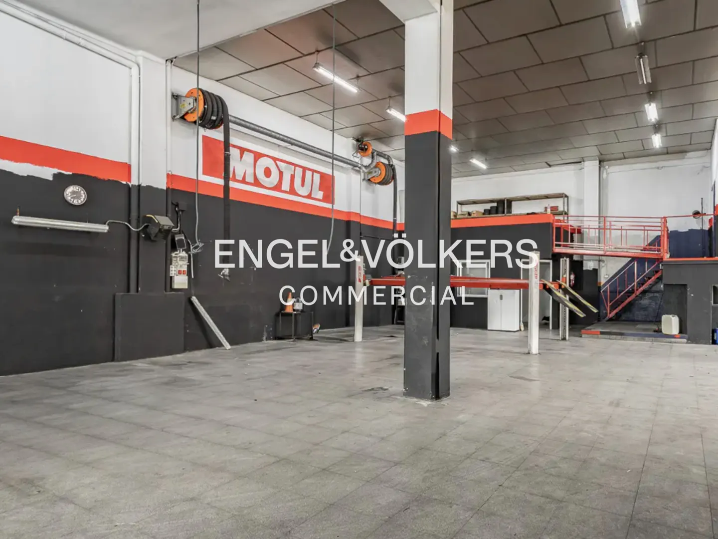A commercial garage space with gray floors, black and white walls with red accents, and car lifts.