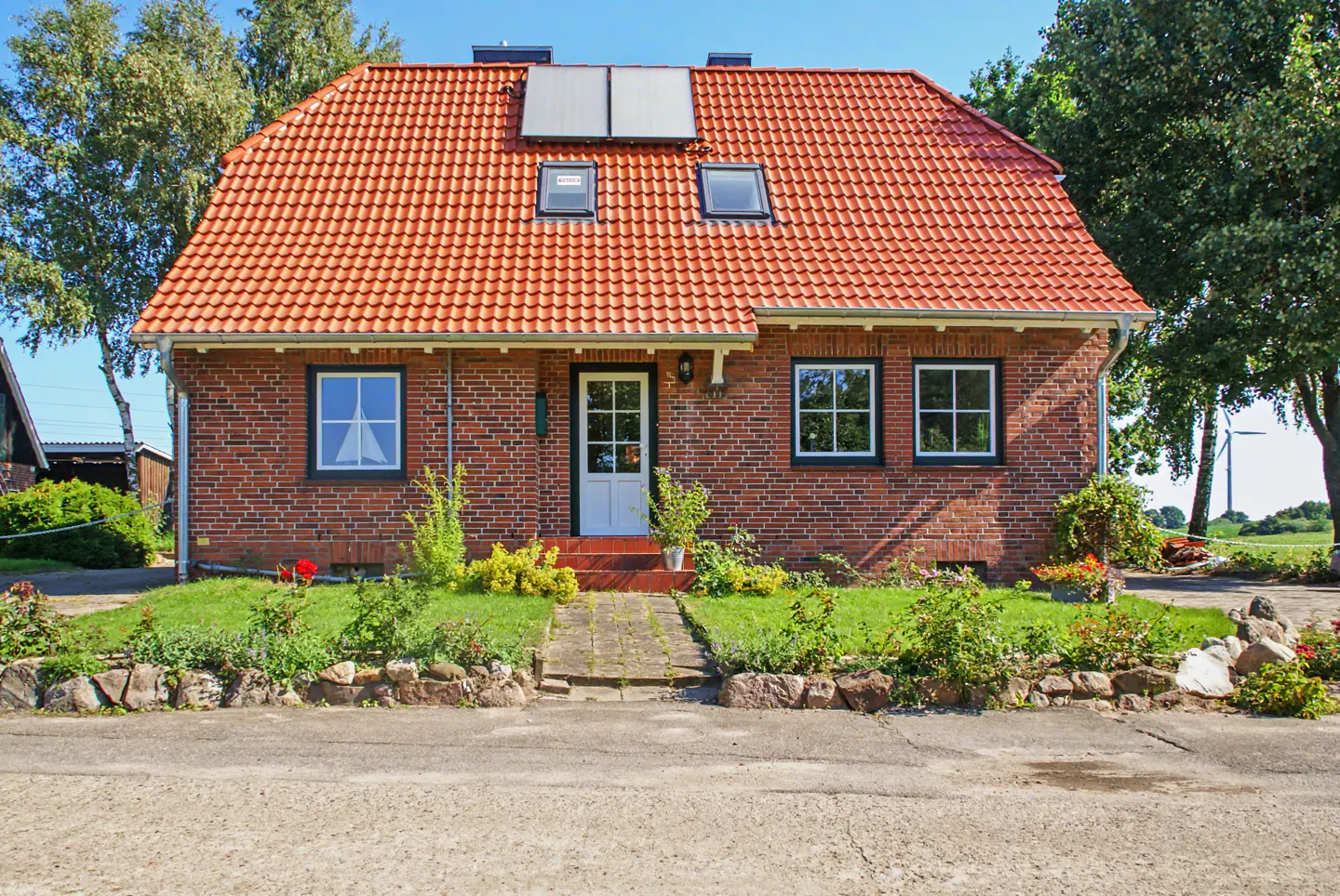 A red brick house with a red tile roof, solar panels, and a white front door.