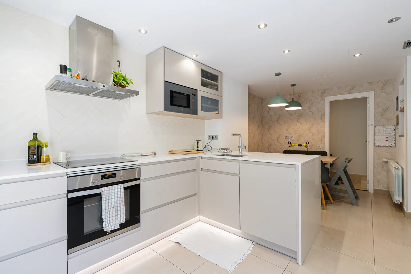 Bright, modern kitchen with white cabinets, stainless steel appliances, and a small dining area visible in the background.