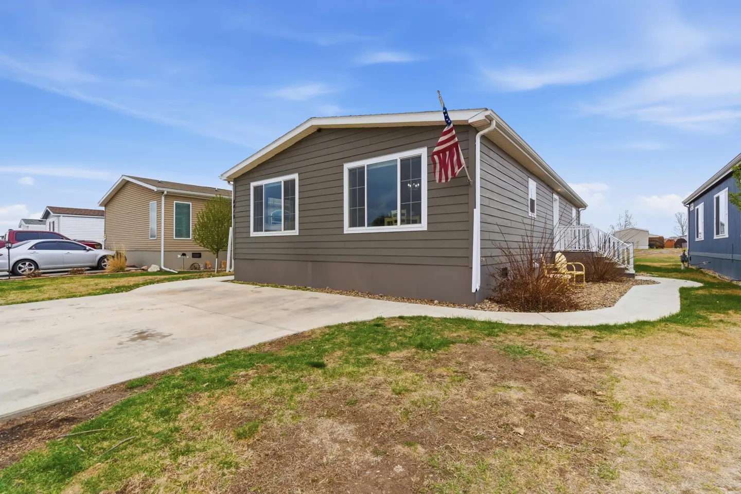 Exterior view of a single-story, gray home with white trim and an American flag. A concrete driveway and walkway lead to the house.