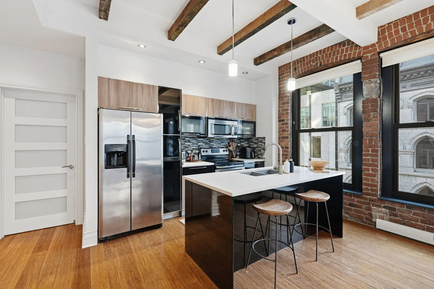 A modern kitchen with stainless steel appliances, a black island with stools, and exposed brick walls.