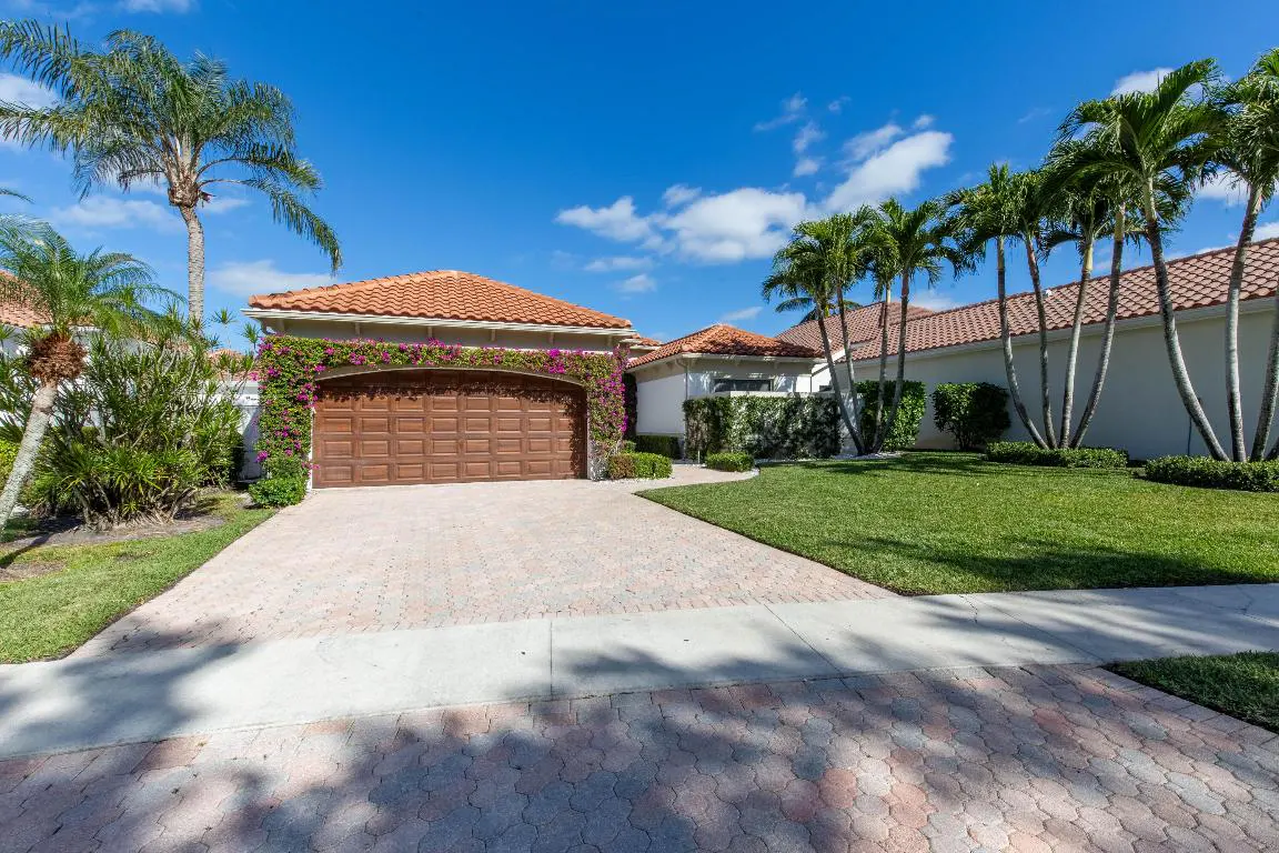 Exterior of a house with a brown garage door, orange tile roof, and palm trees under a blue sky.