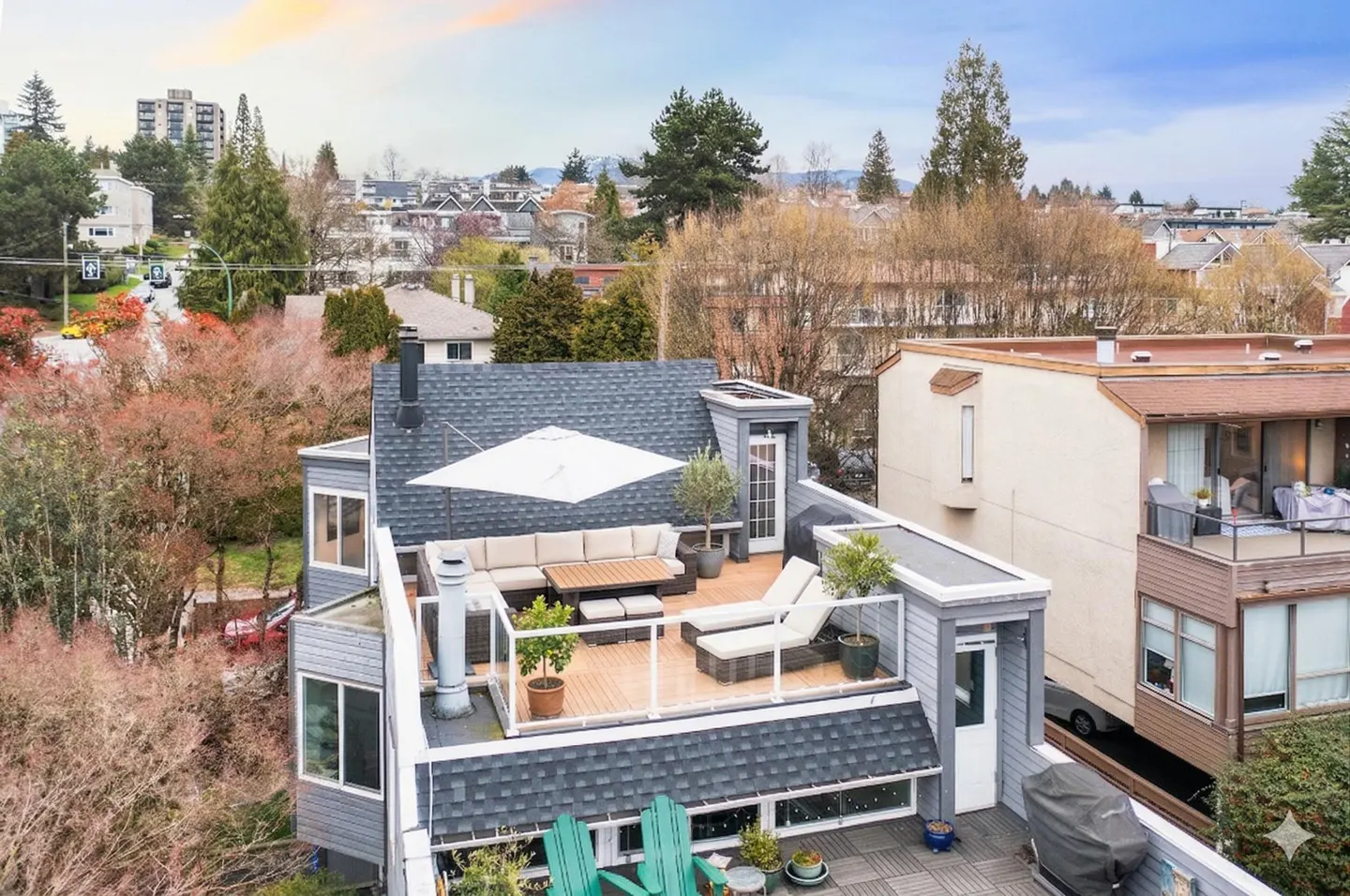 Aerial view of a rooftop deck with outdoor furniture, including a sofa, chairs, and a table, with city views in the background.