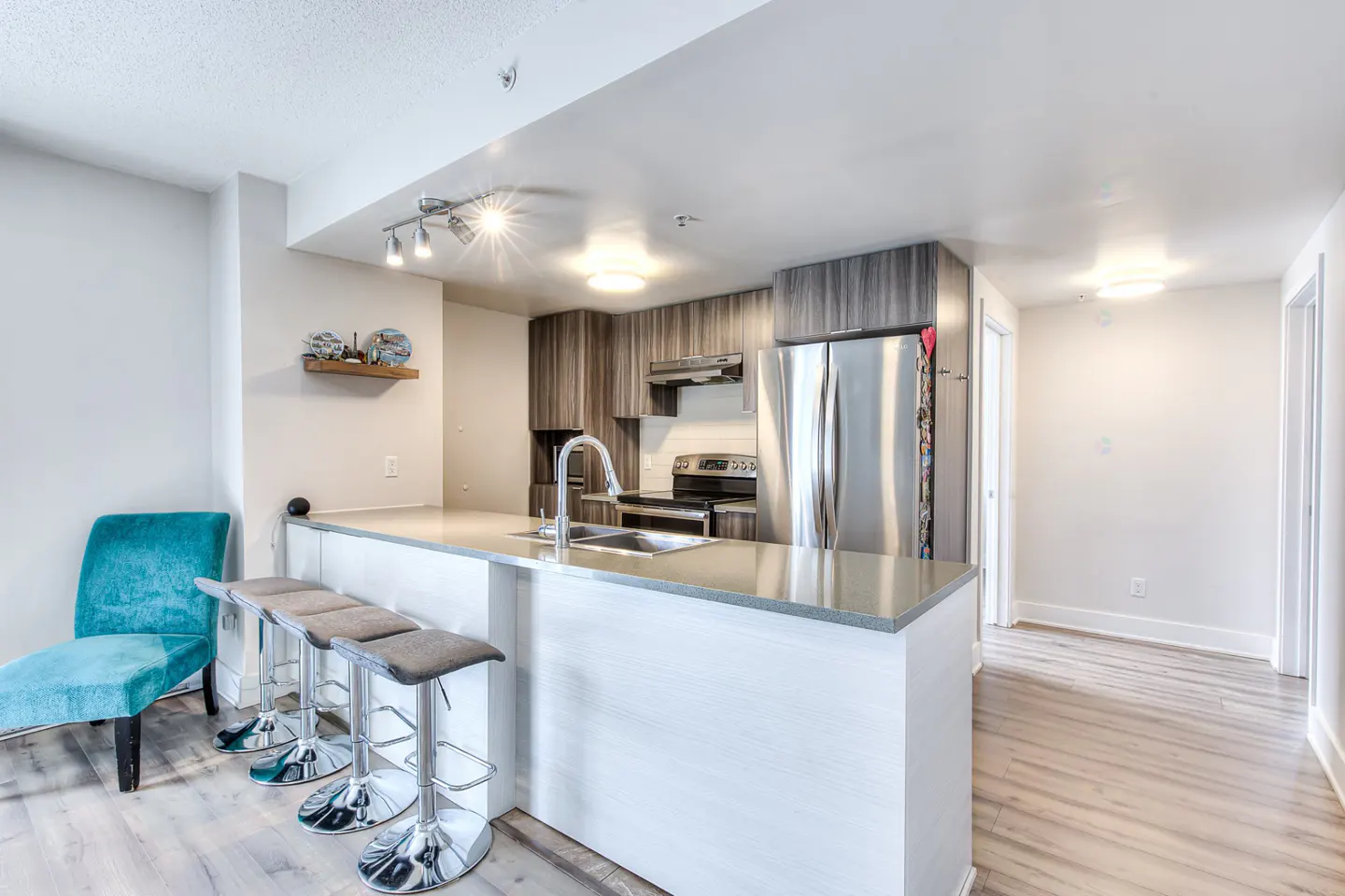Bright, modern kitchen with white island, gray stools, stainless steel appliances, and a turquoise chaise lounge.