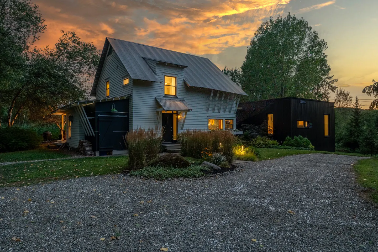 Exterior view of a light blue house with a metal roof and a black modern addition at sunset.