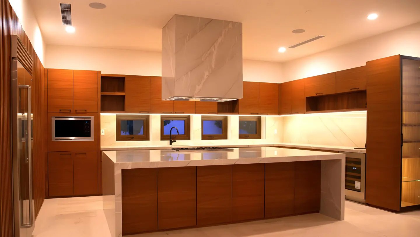 Modern kitchen with warm wood cabinetry, a large marble island, a matching marble range hood, and under-cabinet lighting.