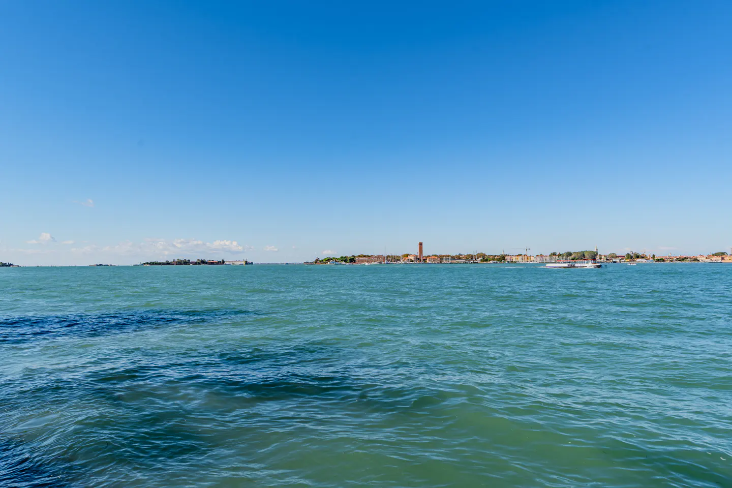 Venice cityscape view from the water. Blue sky, turquoise water, and distant buildings.