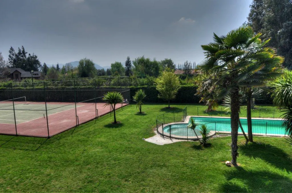An aerial view shows a tennis court and pool in a backyard with palm trees and green grass.