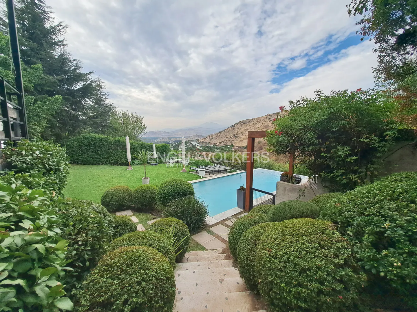 A backyard with a pool, green bushes, and a view of mountains in the distance.