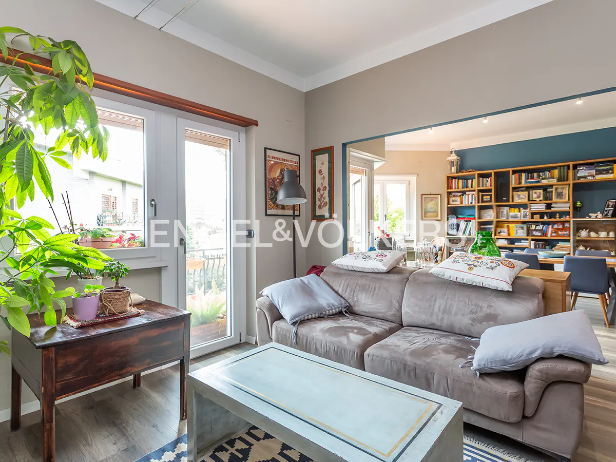 Living room with a gray sofa, light blue coffee table, and a dark wood side table with plants near a window.