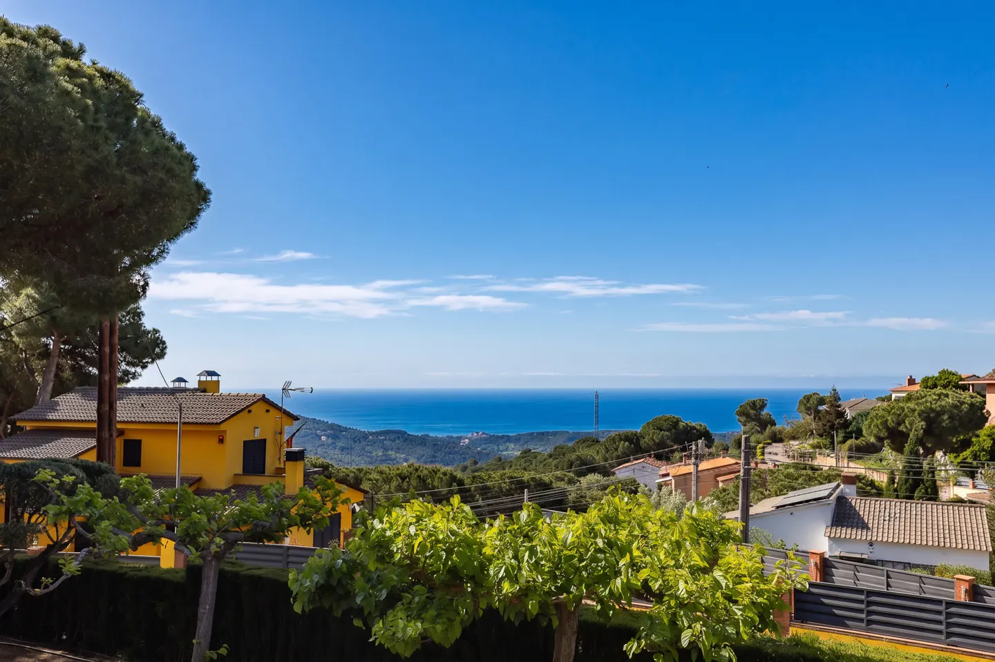 View of a yellow house and other homes with the ocean in the background on a sunny day.