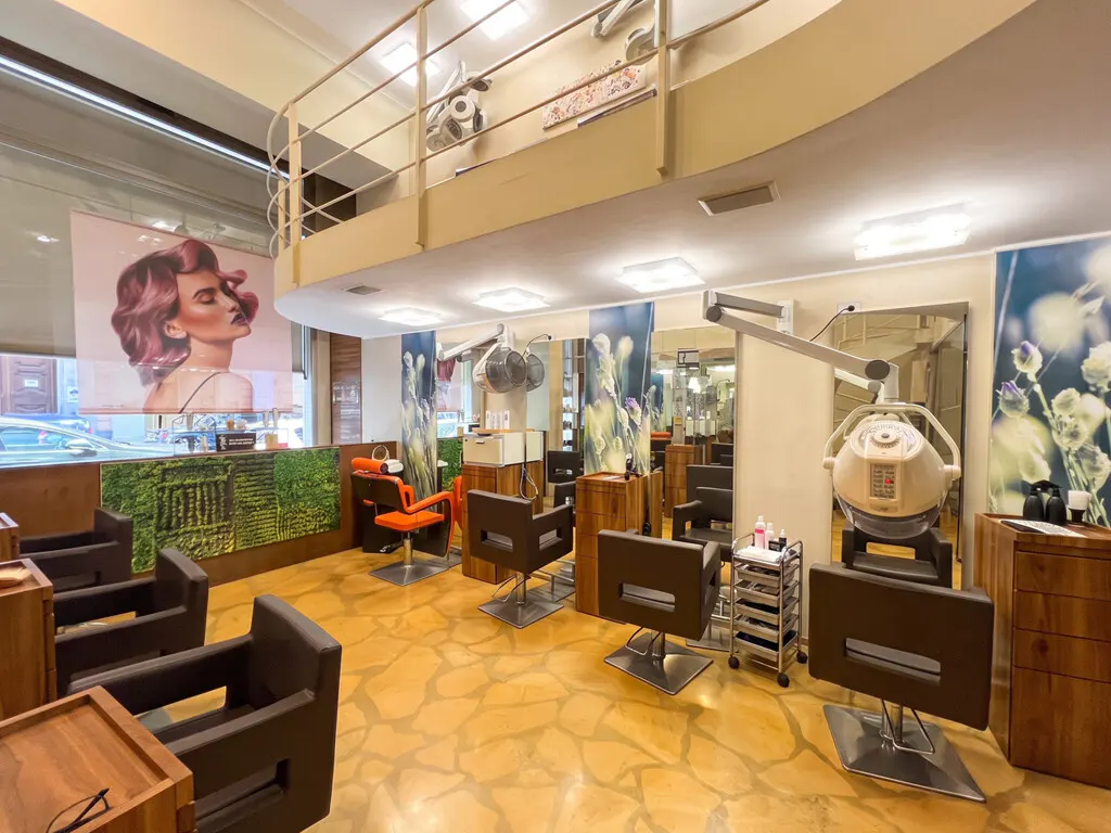 Modern hair salon interior with brown chairs, yellow stone-look flooring, a mezzanine level, and wall art.