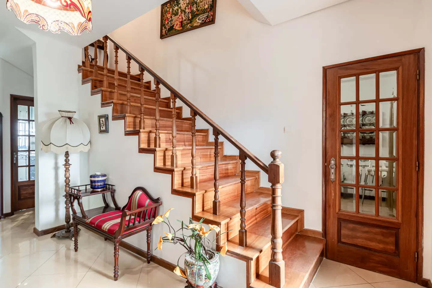 Interior view of a home featuring a wooden staircase, a red striped bench, and a glass-paneled door.