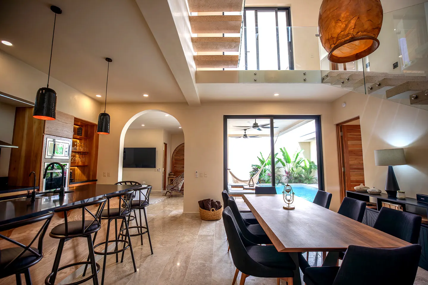 Open-concept living space with kitchen island, dining table, and view of a pool through sliding glass doors.