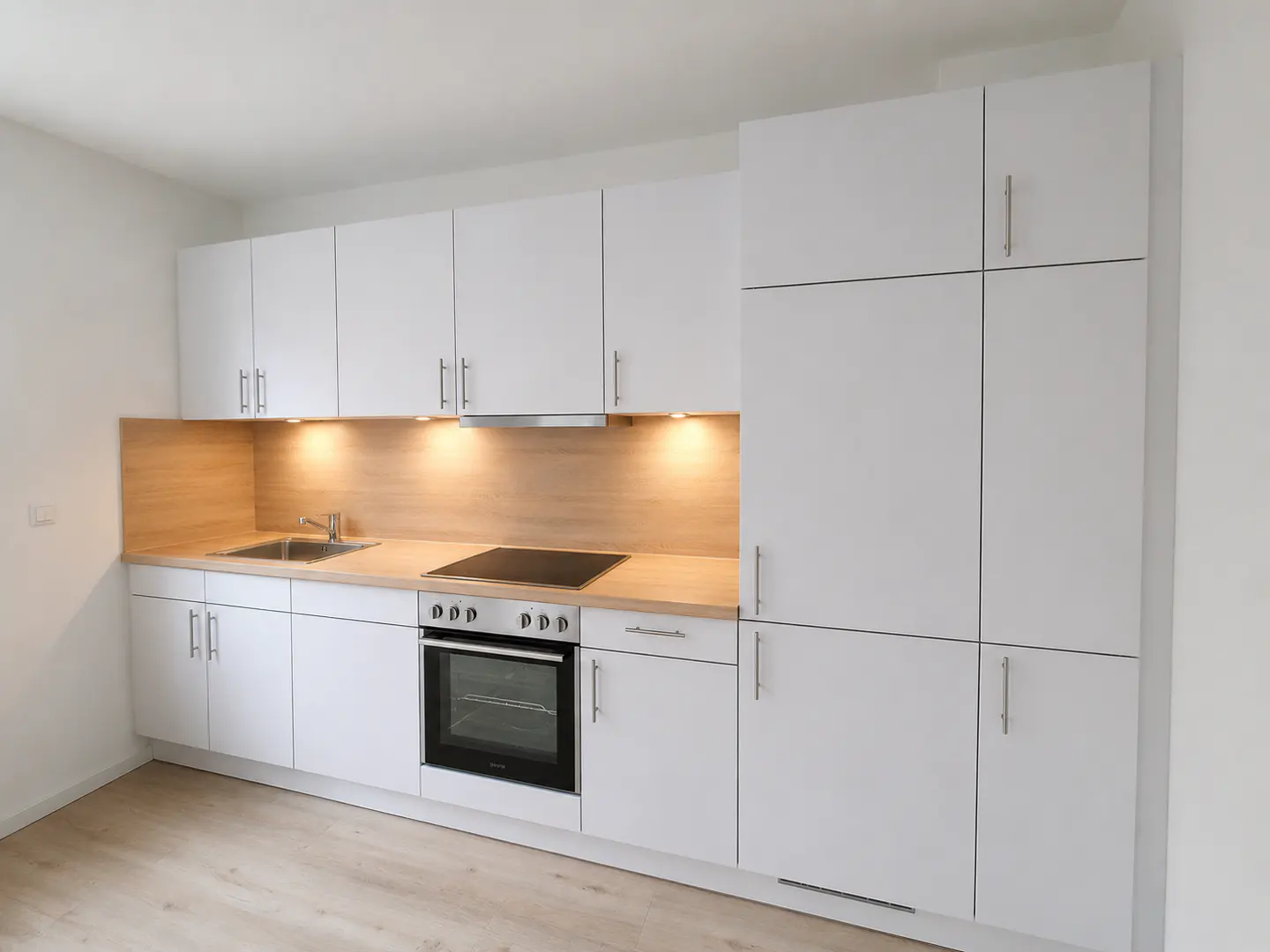 Bright kitchen with white cabinets, wood countertop, stainless steel sink, and oven.