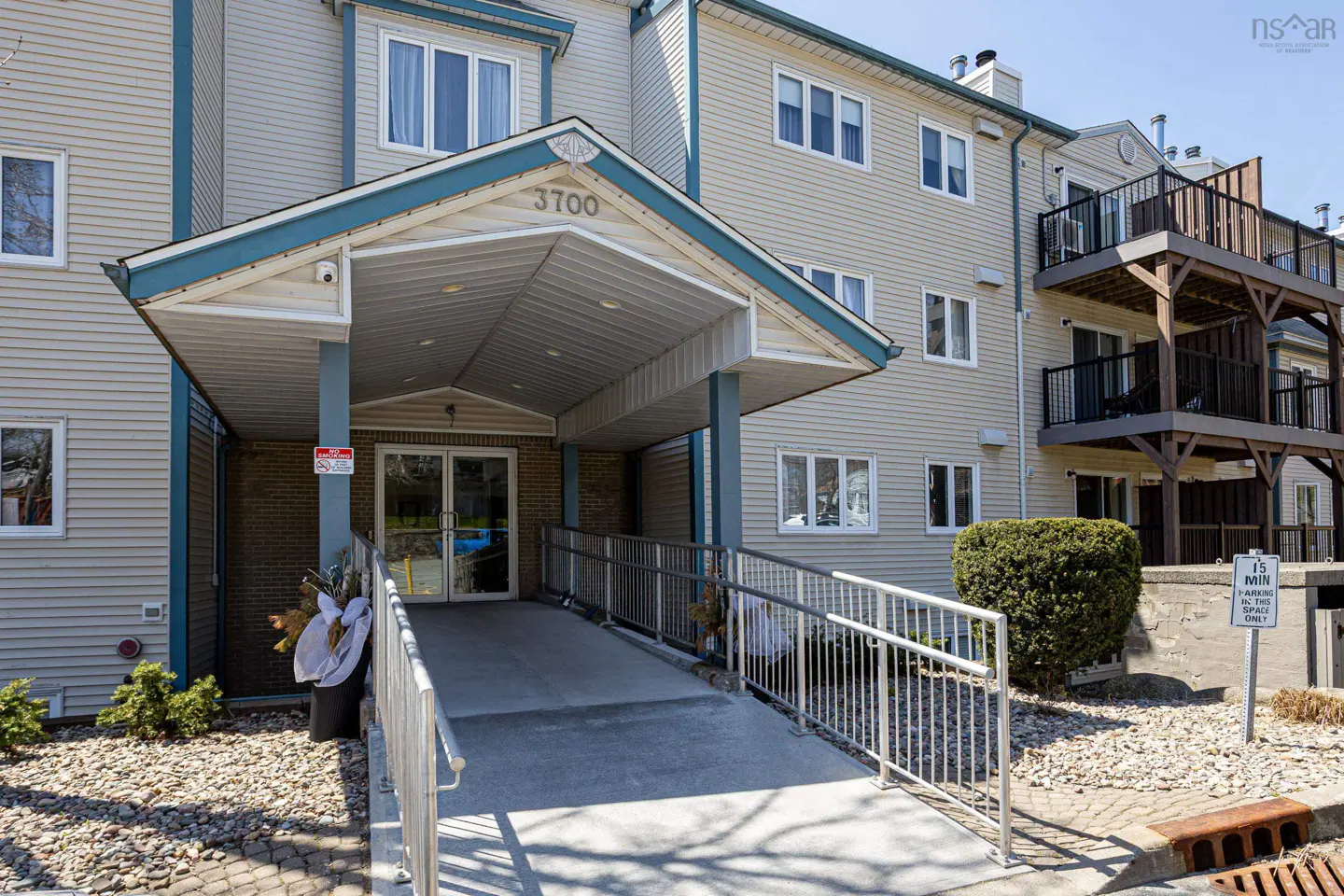 Exterior of a beige apartment building with a ramp leading to the entrance. The building has multiple windows and balconies.
