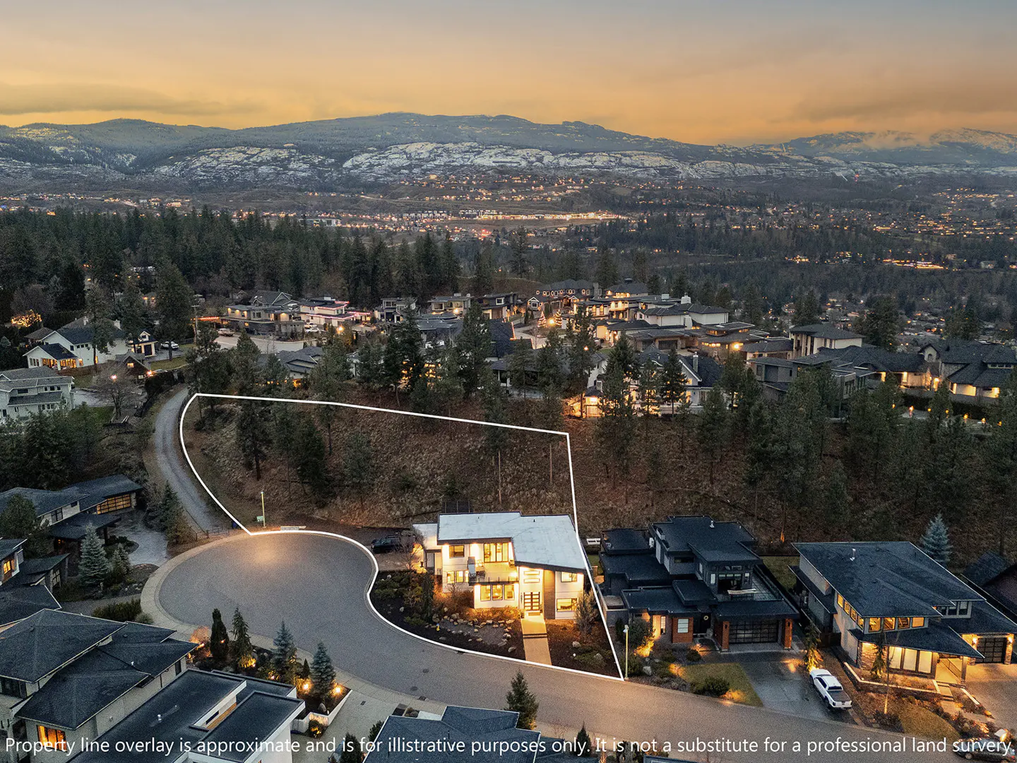 Aerial view of a modern house with a white property line overlay, surrounded by trees and other houses, with mountains in the background.