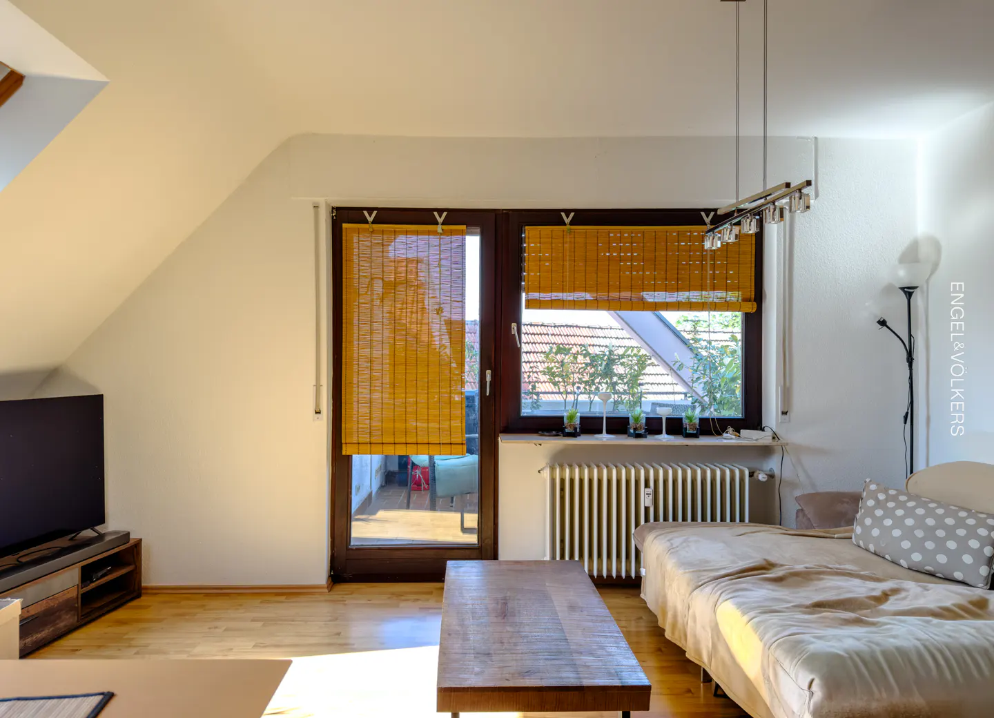 Living room with wood floors, a brown coffee table, and a daybed with a gray polka dot pillow. Windows have bamboo shades.